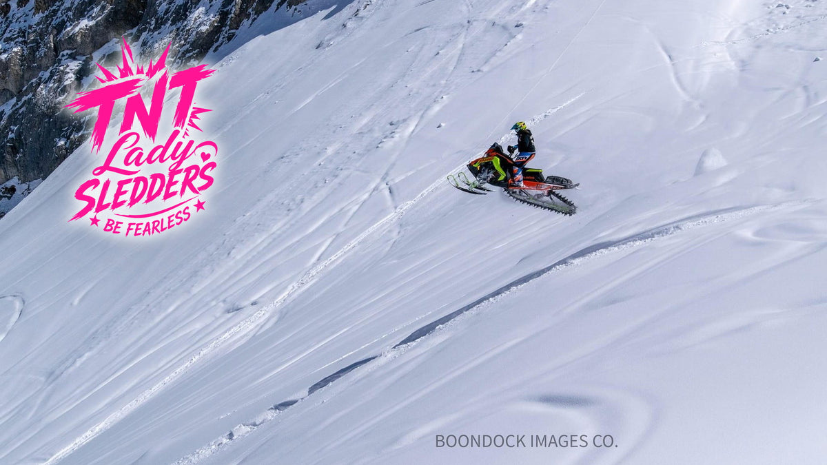 TNT Lady Sledders logo over Gisele sidehilling a steep mountain slope on her sled