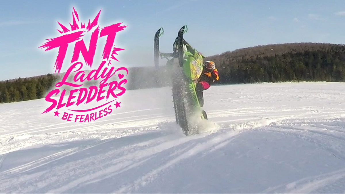 TNT Lady Sledders logo over Sharon pulling a wheelie across a snowfield