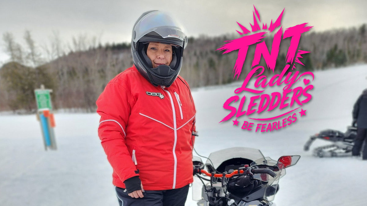 TNT Lady Sledders logo over Denise in a red jacket standing beside her sled on a snowy trail